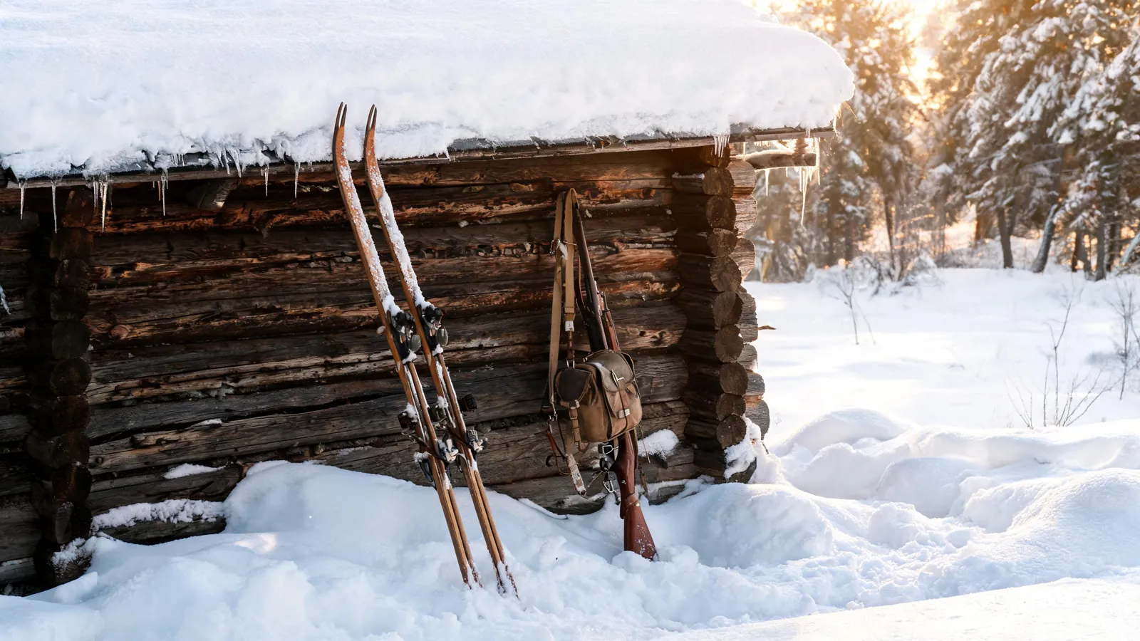 Gamle treski og et skulderbelte ved en tømmervegg i snø